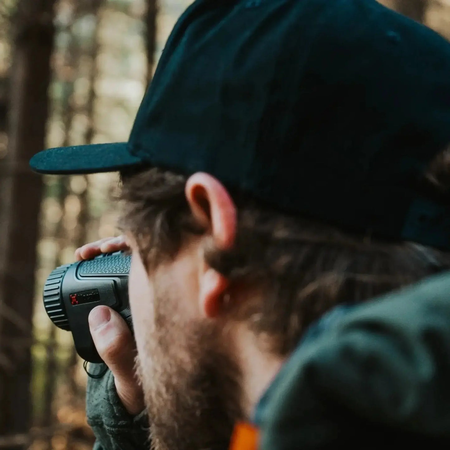 A person wearing a black hat, seen from behind, holding a Nocpix Lumi thermal imaging monocular to their eye, demonstrating its use in the field.
