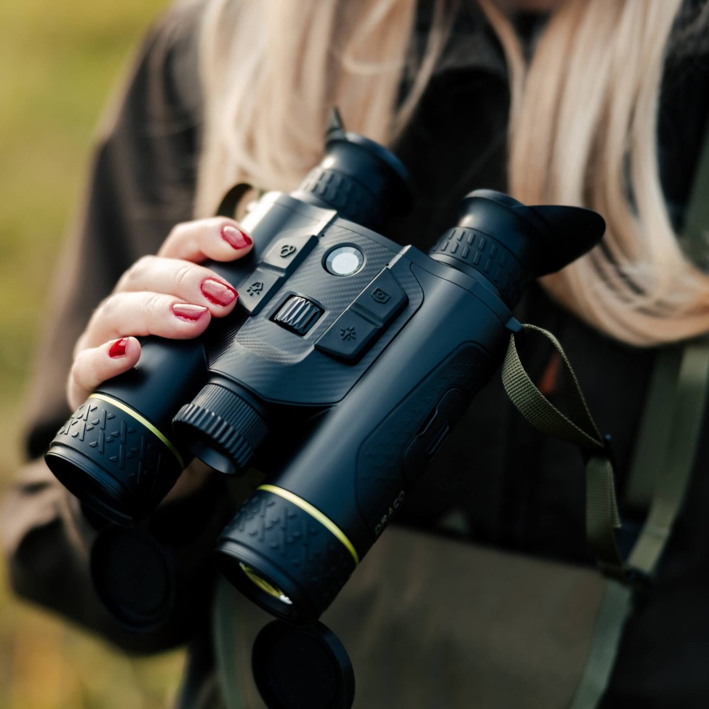 Close-up view of a model holding the Pixfra Draco D335-4K Multispectral Binoculars, demonstrating the device's compact, traditional binocular ergonomics. The image highlights the rugged black housing, the intuitive multi-function wheel near the model's hand, and the distinct dual-lens system featuring a 35mm thermal lens and 4K night vision lens with green ring accents.