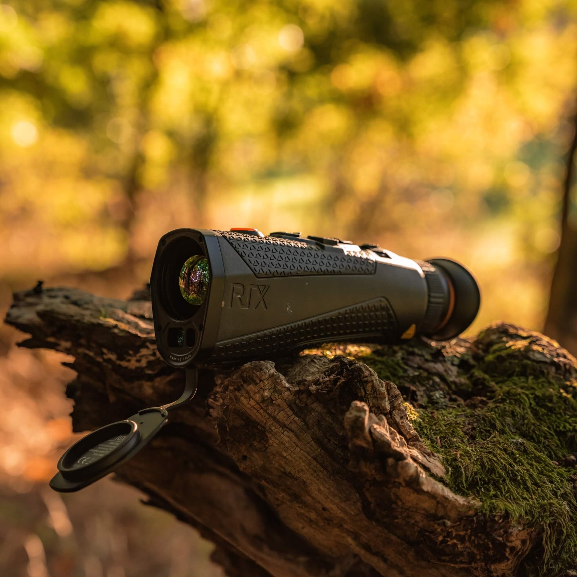 RIX Titan T3 Thermal Monocular positioned in a wooded area on an old piece of wood, highlighting its compact ergonomics and 25mm F0.9 objective lens for high-clarity outdoor observation.