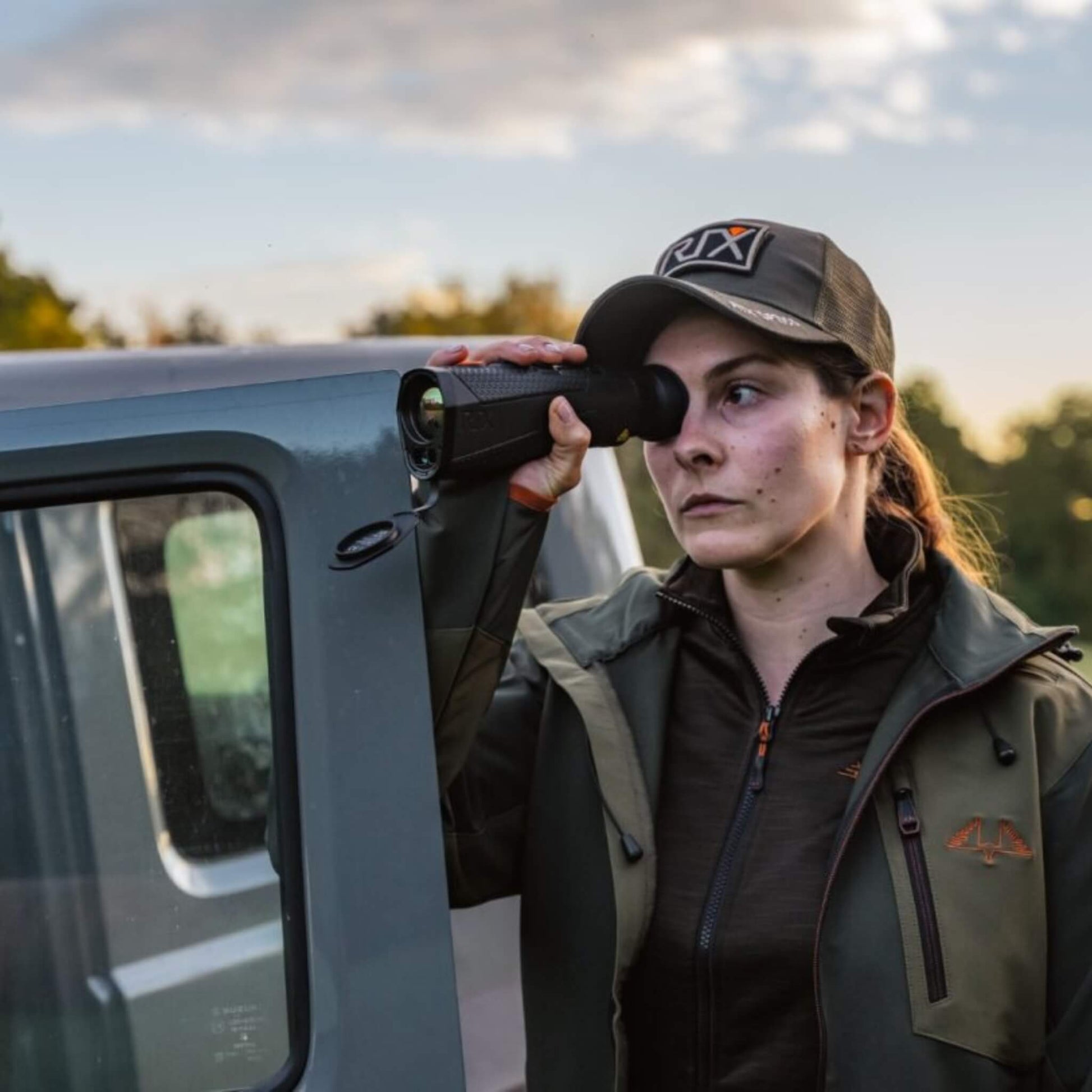 RIX Titan T6 Thermal Monocular held by a lady leaning her forearm on a car door, demonstrating the device's stability and portability for mobile surveillance or quick-access field diagnostics.