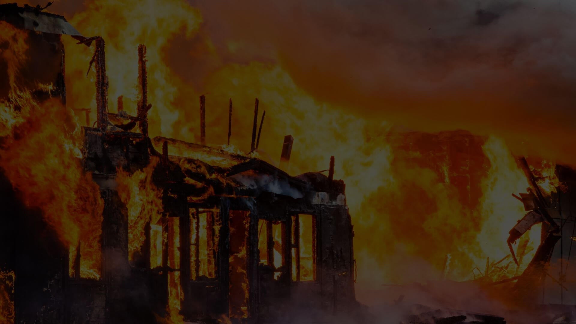 A dramatic nighttime photograph of a large industrial building completely engulfed in massive flames, illustrating the catastrophic consequences of delayed fire detection that radiometric thermal camera systems are designed to prevent.